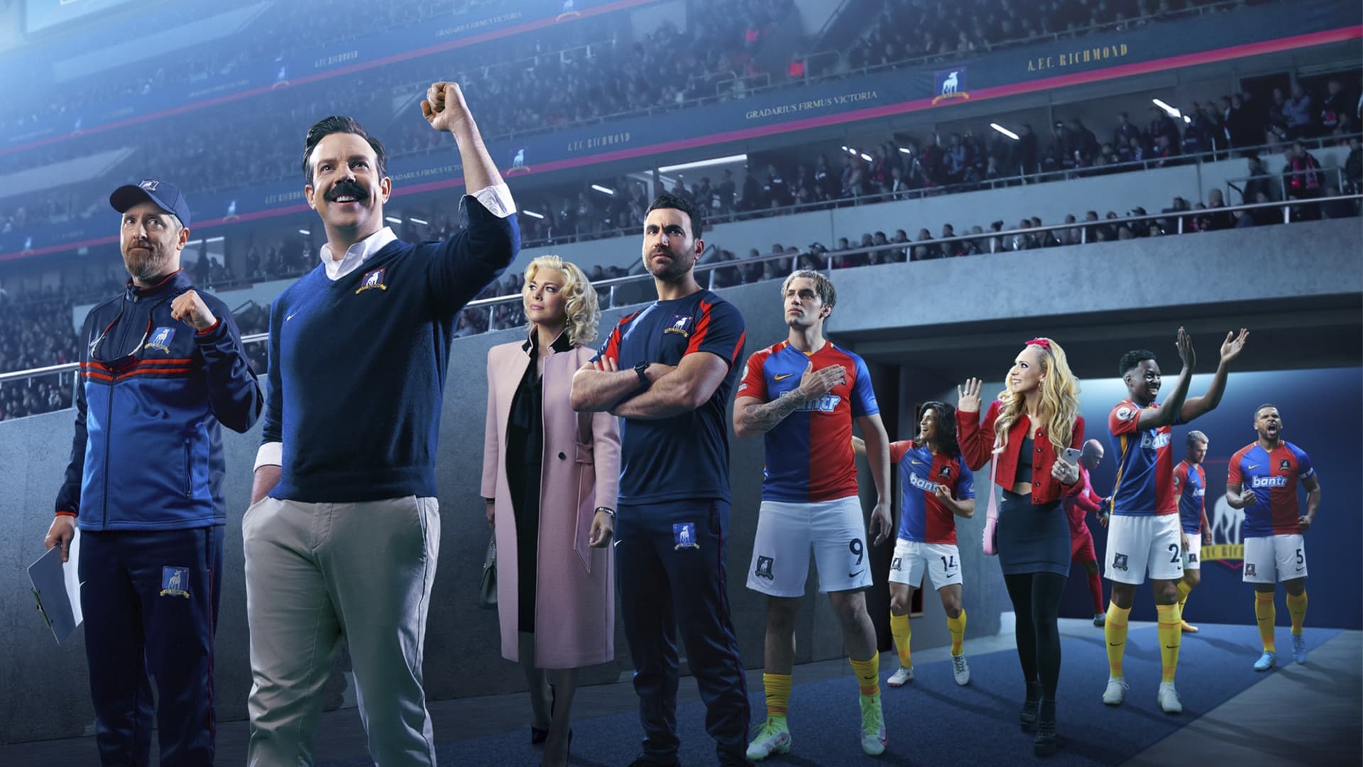 Eine Gruppe diverser Menschen läuft in ein Fußballstadion ein. Es sind die Charaktere aus Ted Lasso.